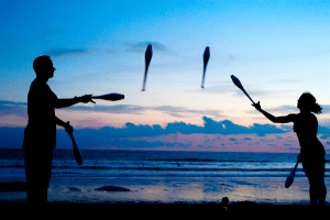 Man and woman juggling on a beach at sunset.