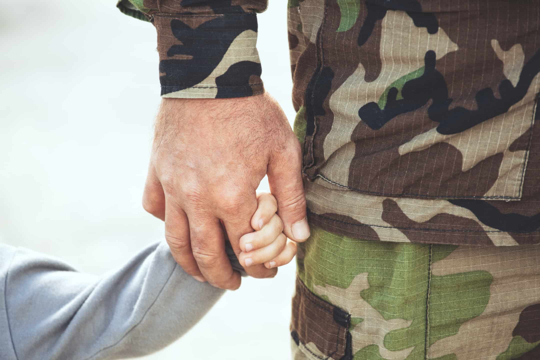 Child holding father's hand who is dressed in military camo