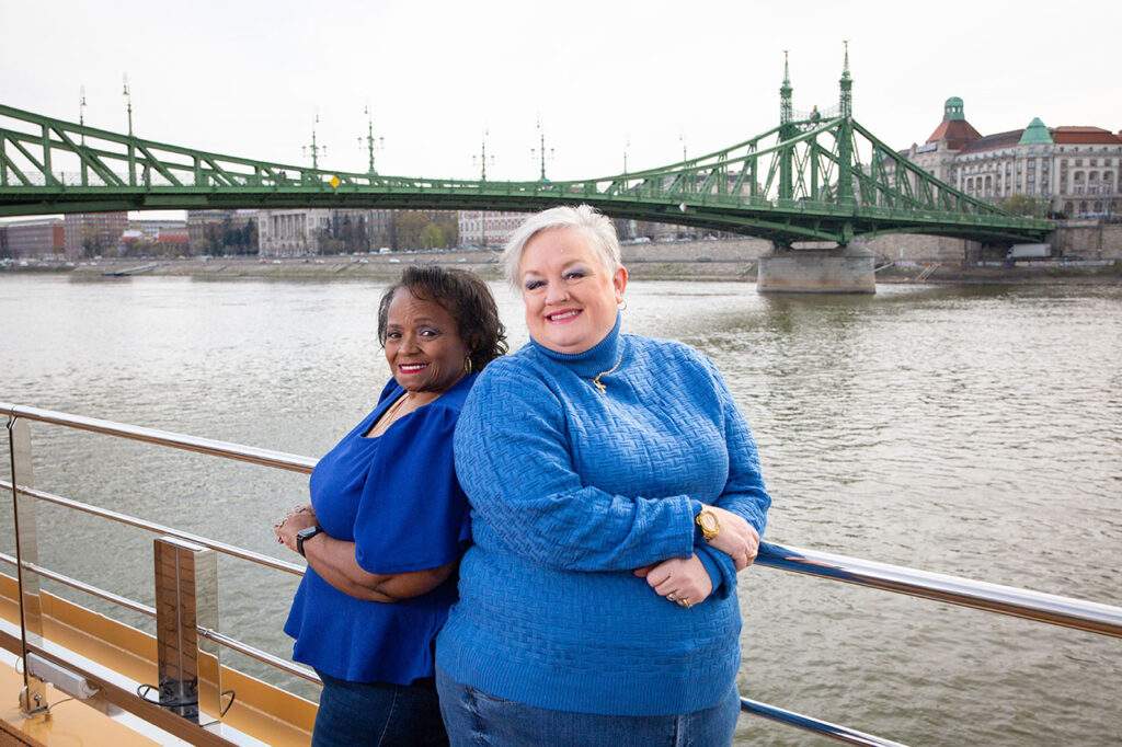 two Dream Vacations travel agents with a bridge behind them
