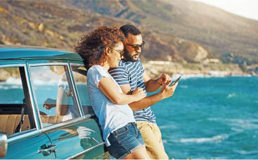 A couple leaning on a car along the ocean