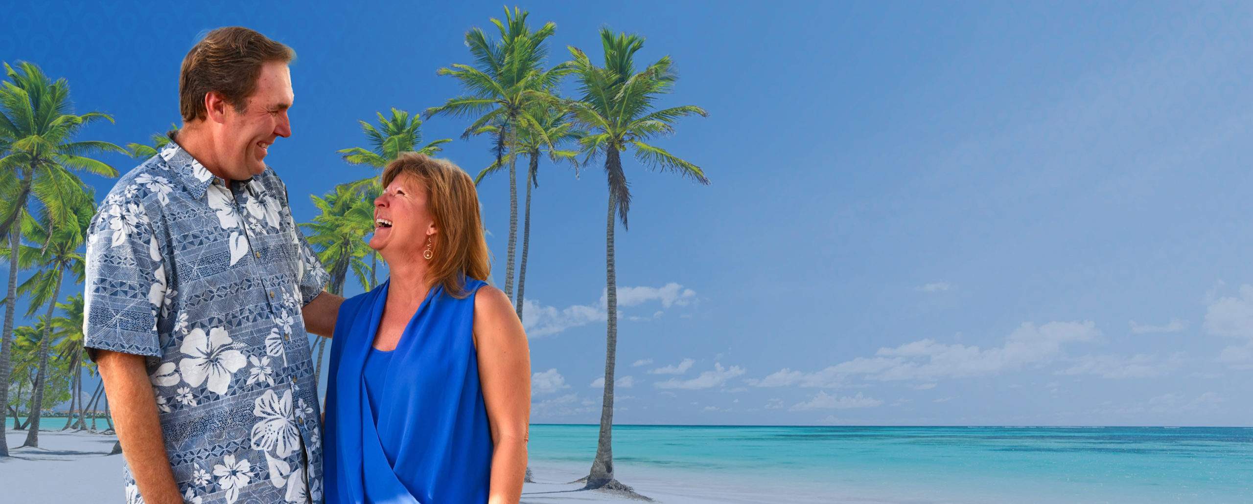 A couple on a sunny beach smiling at one another