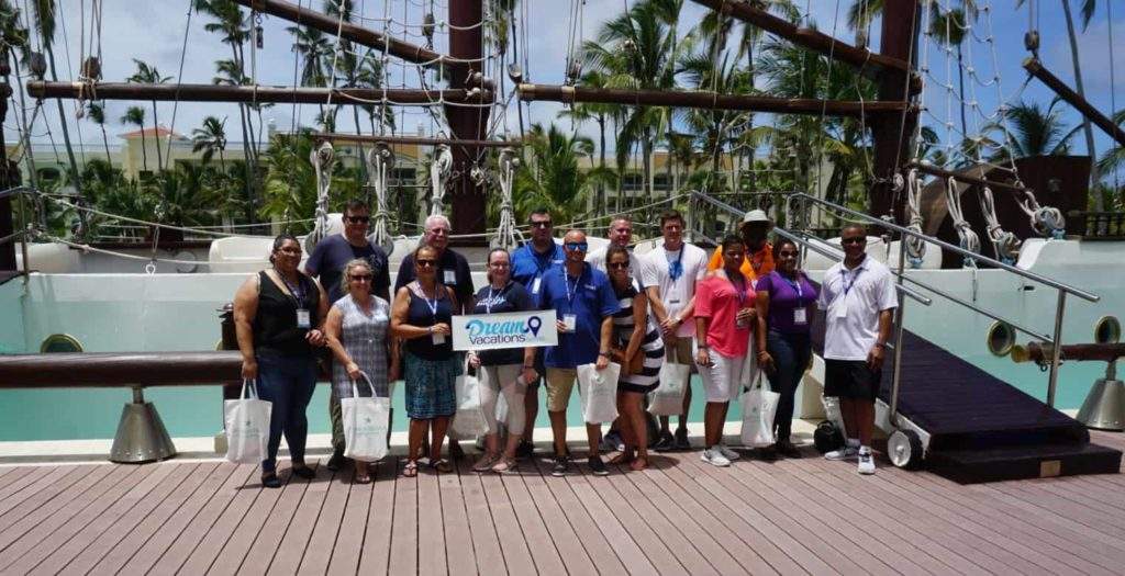 Team members holding a Dream Vacations banner - learn your our travel agency marketing strategy