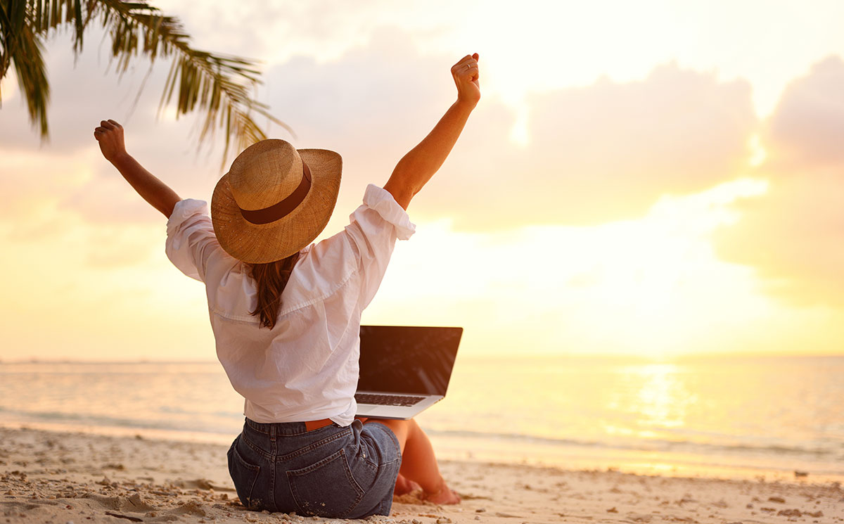 Woman with laptop on beach, perhaps pondering the question: 'Should I Buy a Travel Franchise?'