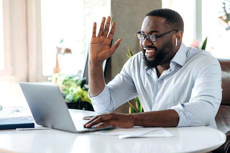 Man on laptop smiling and waving at webcam - learn tips for travel agency business owners