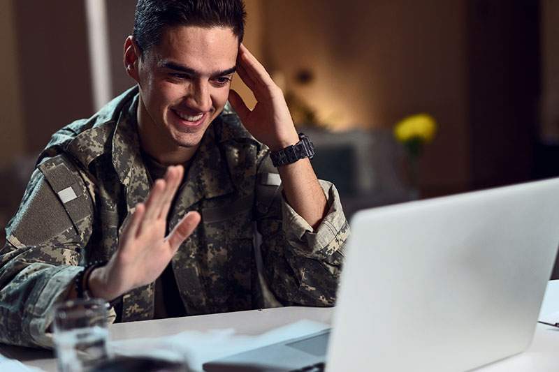 Man in military fatigues smiling at laptop - what are the most affordable franchises for veterans?