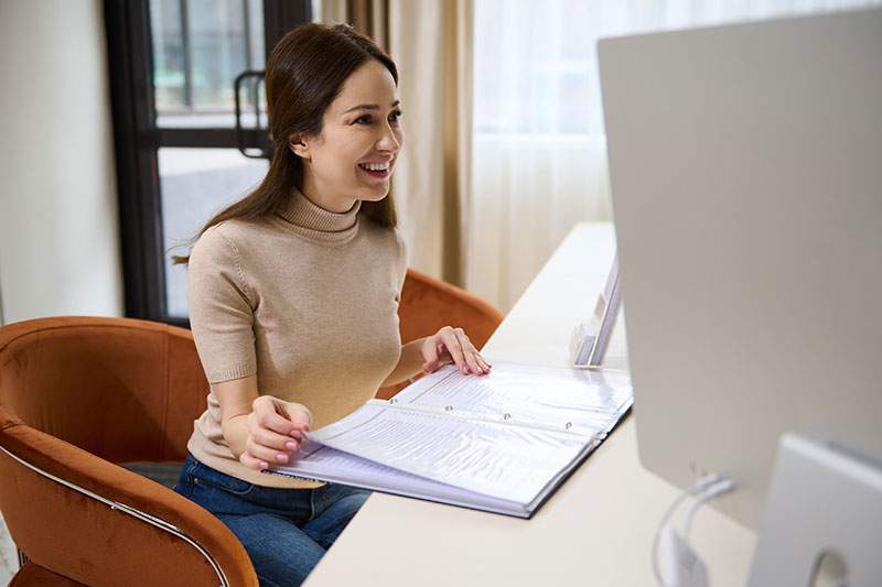 Woman with binder smiling at someone out of frame - how much does it cost to start a travel agency?