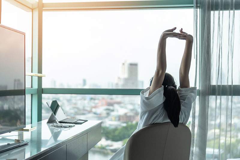 Woman stretching in office, looking out at city - what's the best travel agency franchise to own?