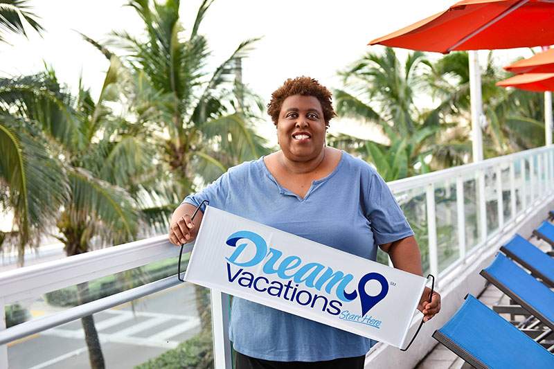 A Dream Vacations Franchise Owner holding a branded banner by the pool - what is a travel franchise?