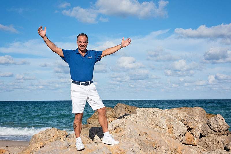 man standing on rocks at the beach with arms raised thinking dream vacations best franchises to own