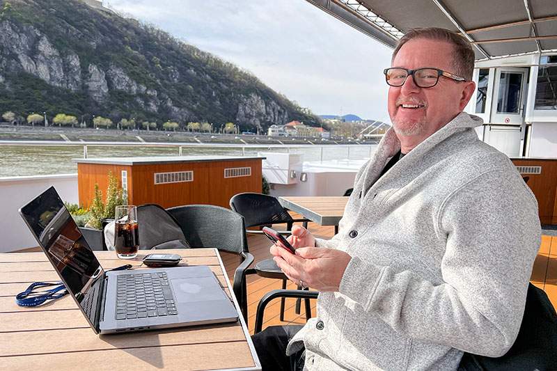 man sitting on a deck of a boat, laughing, with a laptop out - business strategy for travel agency