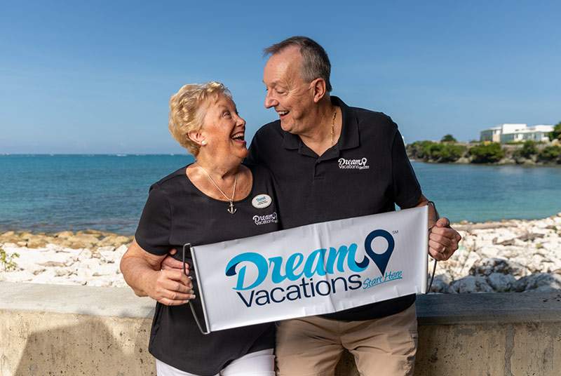 man and women at the beach with Dream Vacations sign