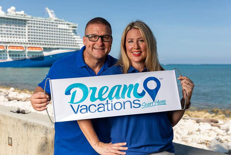 man and woman with Dream Vacations sign with a cruise ship behind them