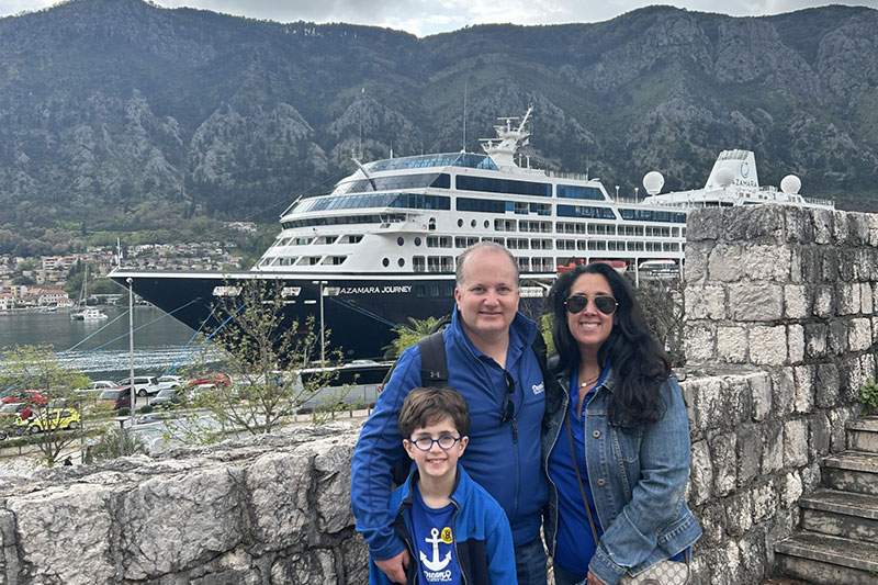 dad, mom, son with a cruise ship behind them