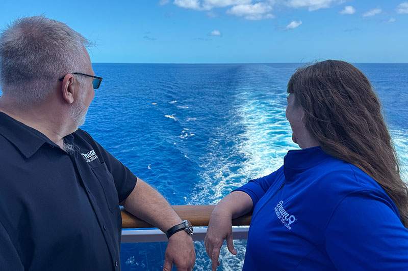 A man and woman stand together on the deck of a cruise ship, enjoying the view of the ocean.