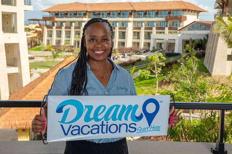 A woman smiles while holding a sign that reads "Dream Vacations"