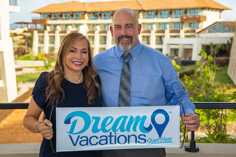 A man and woman joyfully hold a sign that reads "Dream Vacations"