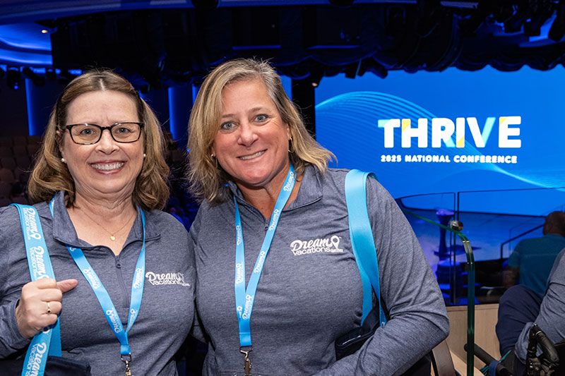 Two women in grey shirts standing side by side smiling